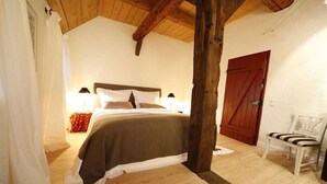 A bedroom with a wooden ceiling, a bed with white and brown bedding, a wooden chair, and a red door. - Holiday home in Hanstedt with swimming pool (Hanstedt)