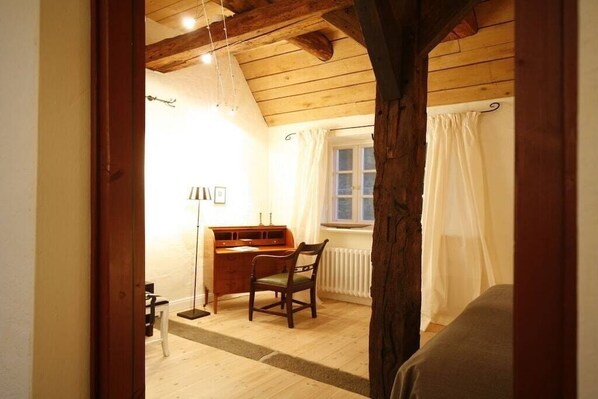 Ein Zimmer mit Holzboden, einem Schreibtisch mit Stuhl, einer Heizung und einem Fenster mit Vorhängen.