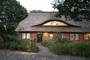 Ein traditionelles Haus mit Strohdach, einer Ziegel-Fassade, einer Haustür und einem Weg zum Eingang.