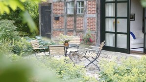 A traditional building with a brick facade, a wooden door, and a window. There is a small outdoor seating area with a table and chairs. - Holiday home in Hanstedt with swimming pool (Hanstedt)