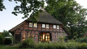 A traditional brick house with a thatched roof, a large arched doorway, and a well-maintained garden. - Holiday home in Hanstedt with swimming pool (Hanstedt)