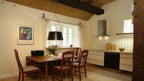 A dining area with a wooden table and chairs, a black pendant light, and a window with curtains. - Holiday home in Hanstedt with swimming pool (Hanstedt)
