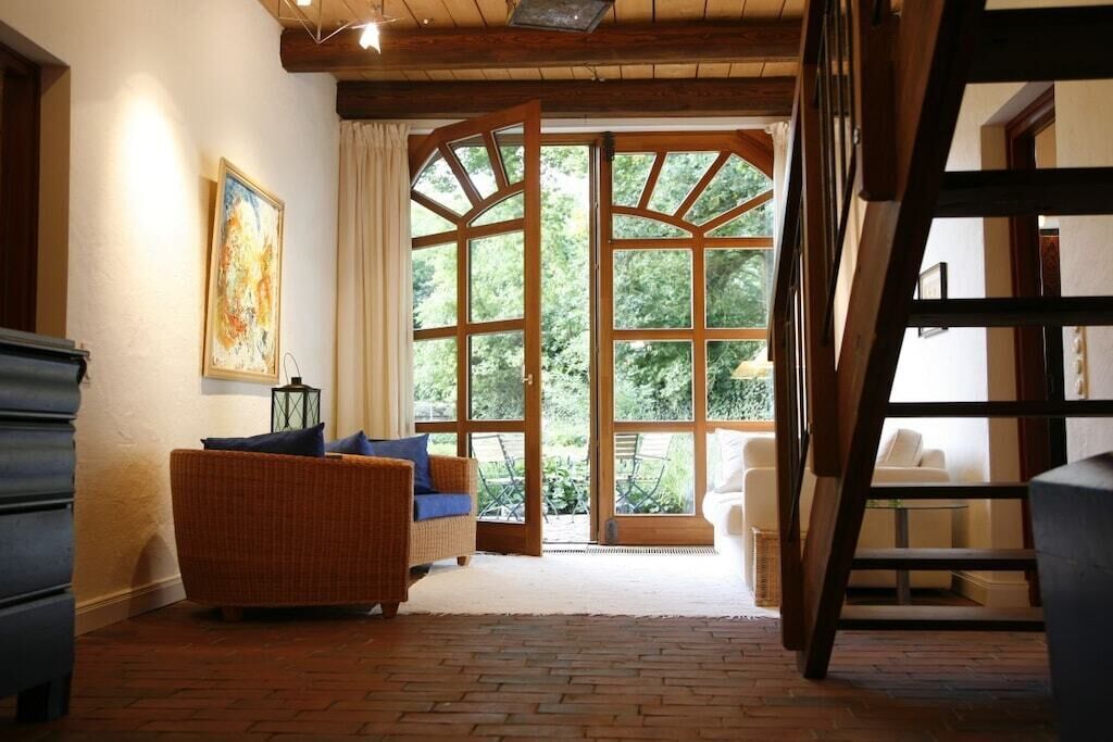 A room with a wicker sofa, a white armchair, and a wooden staircase.