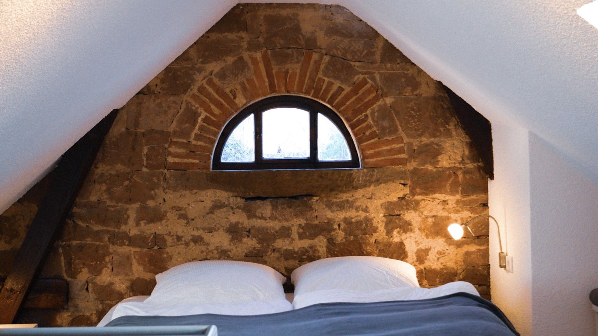 Een slaapkamer met een stenen plafond, een raam en een bed met wit beddengoed.