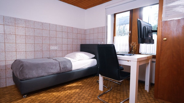 Una habitación pequeña con una cama, un escritorio y una televisión.