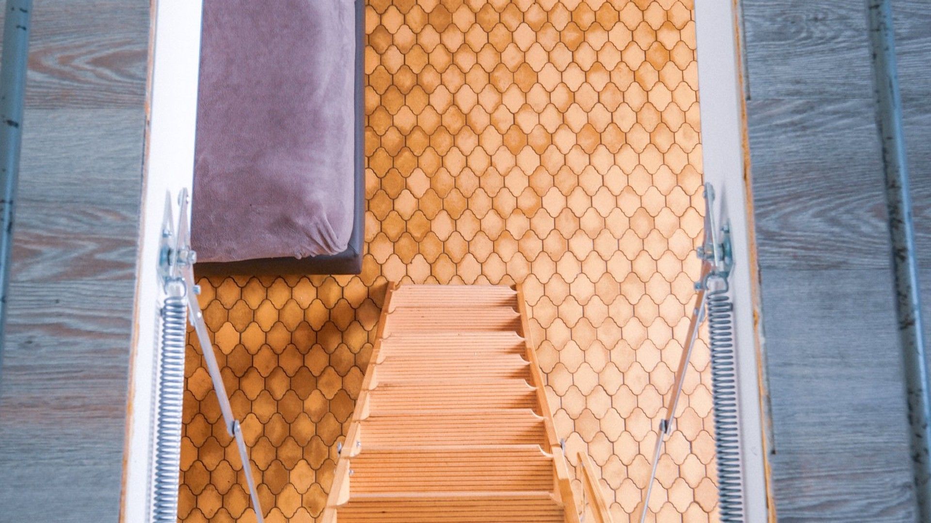 Un escalier en bois, avec un mur orné d’un motif en nid-d’abeille et une serviette violette sur le côté gauche.
