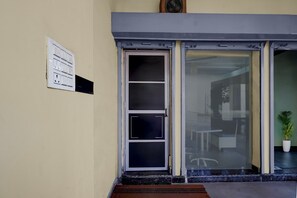 A hotel entrance with a door, a wall-mounted light switch, and a potted plant.