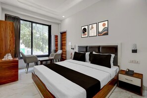 A modern hotel room with a large bed, a desk, a chair, and a window with curtains.