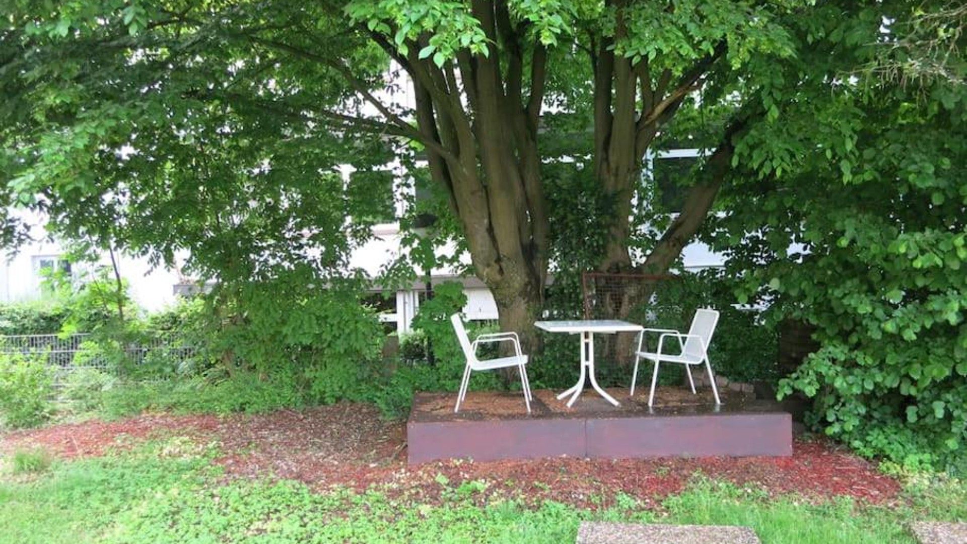 Ein Sitzbereich im Freien mit Tisch und Stühlen unter einem Baum.