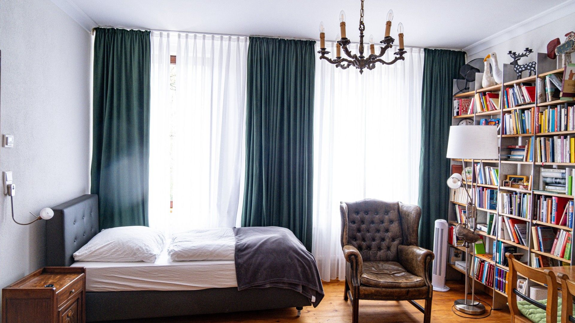 Ein Schlafzimmer mit Bett, einem Sessel, einem Bücherregal und einer Deckenleuchte.