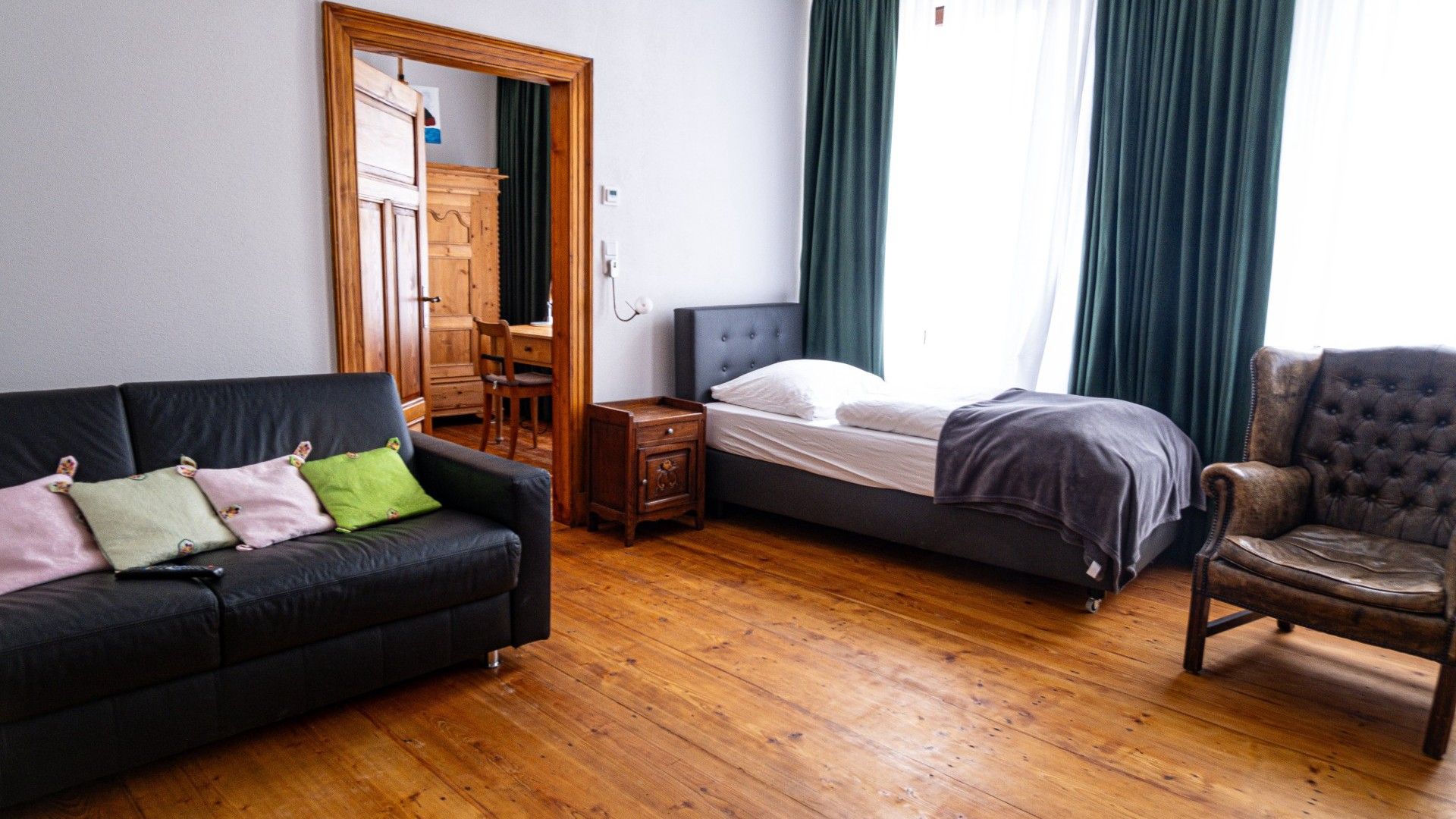Habitació amb llit, sofà, cadira, calaixera de fusta i mirall.