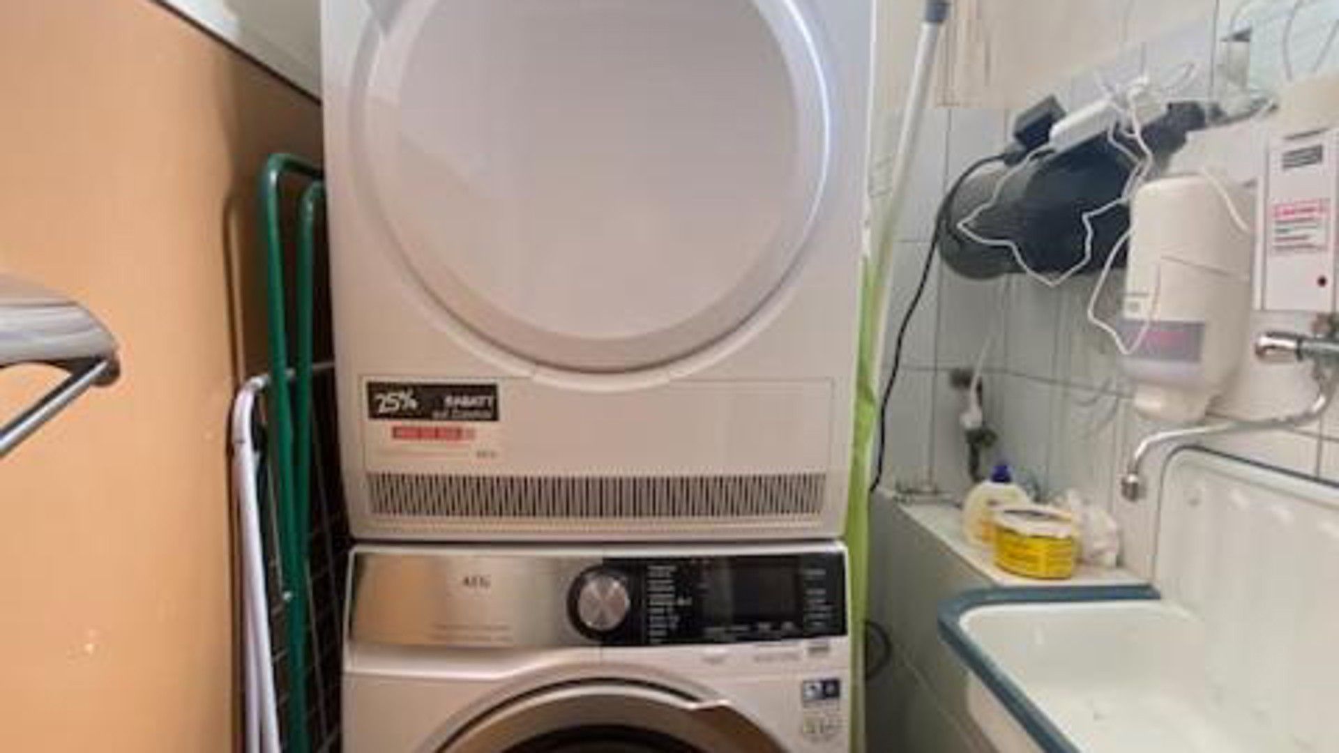 Ein kleiner Waschraum mit Waschmaschine und Trockner, einer grünen Handstange und einer gefliesten Wand.