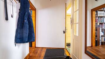 A hallway with a coat rack, a door leading to a room, and a bookshelf.