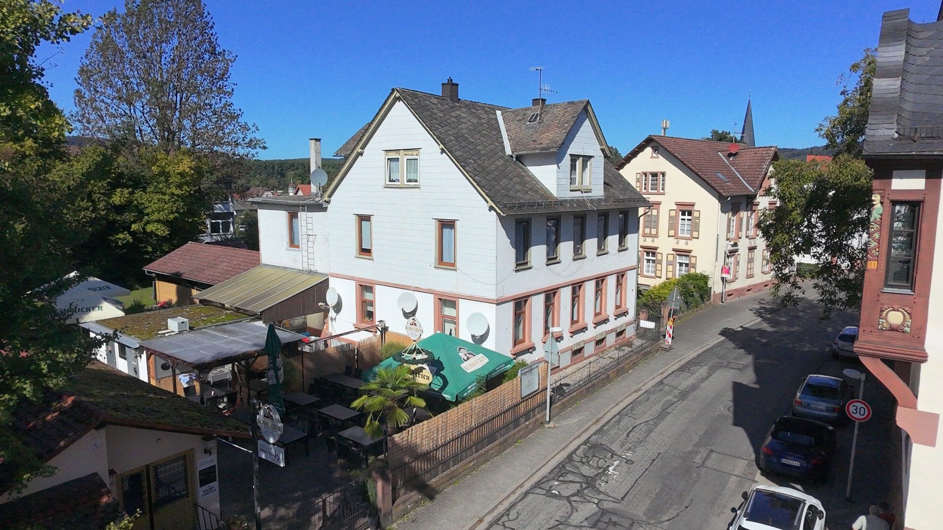 A street view with traditional European architecture, including a two-story building with a sloped roof and a smaller adjacent building with a gabled roof.