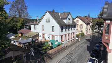 A street view with traditional European architecture, including a two-story building with a sloped roof and a smaller adjacent building with a gabled roof.
