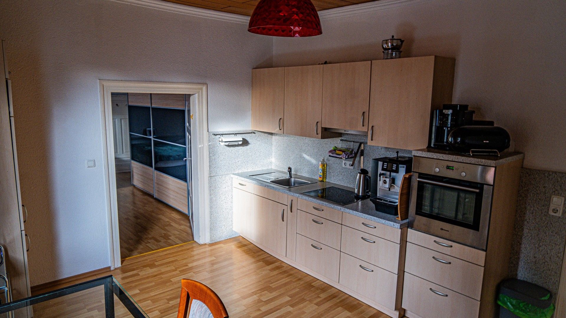 A compact kitchen with wooden cabinets, a built-in oven, and a coffee machine.