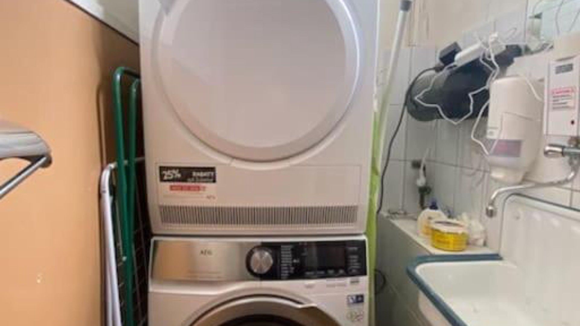A compact laundry room with a washing machine and dryer, a green metal handrail, and a tiled wall.