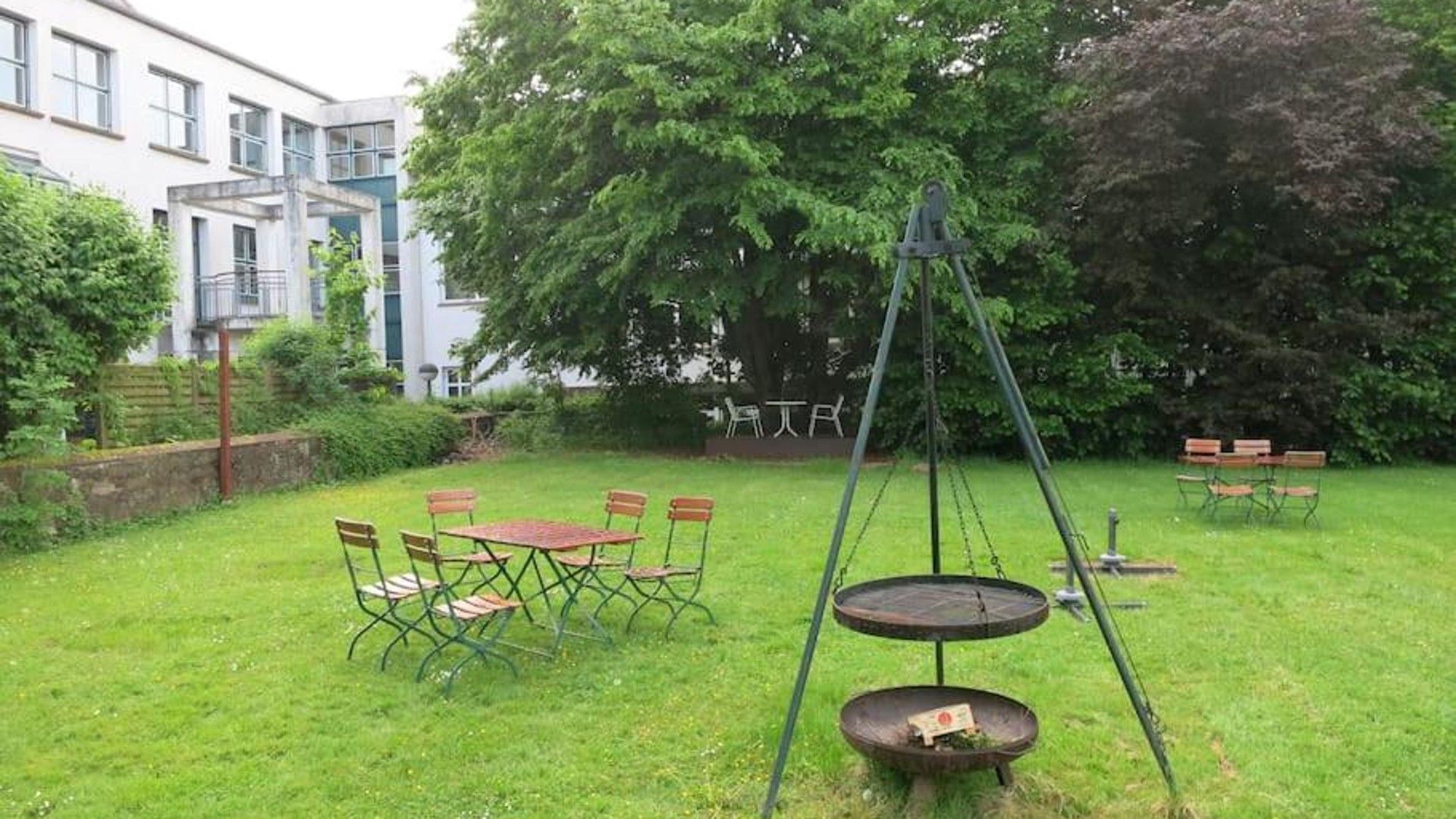 A grassy outdoor area with a swing set, a round table, and chairs.