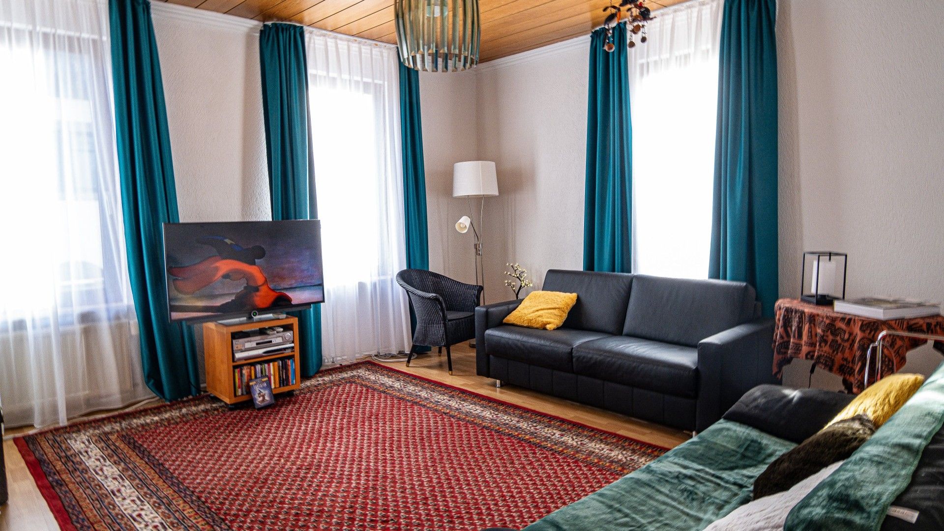 Ein Wohnzimmer mit einer Couch, einem Fernseher, einem Bücherregal und einem gemusterten Teppich.