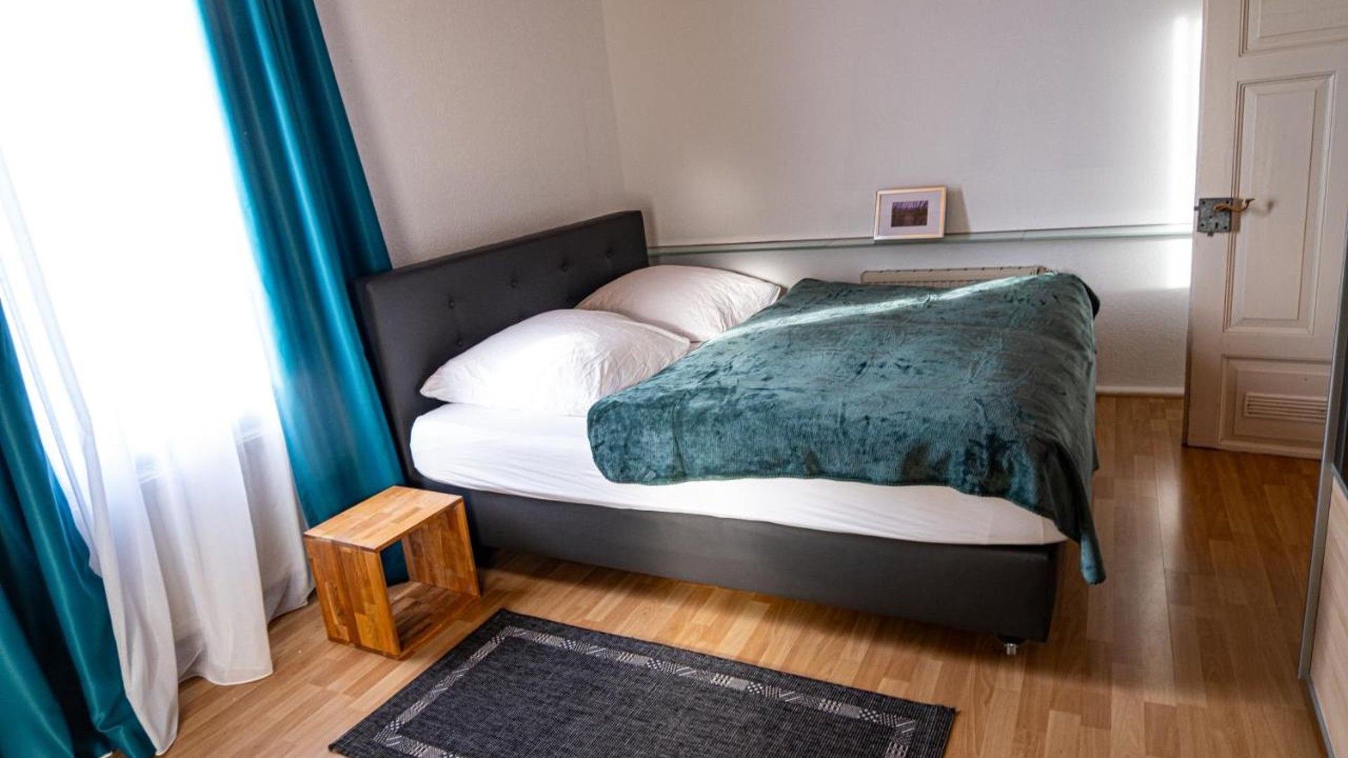 Ein Schlafzimmer mit einem Bett, einem kleinen Holzhocker, einem Teppich und einer Tür.