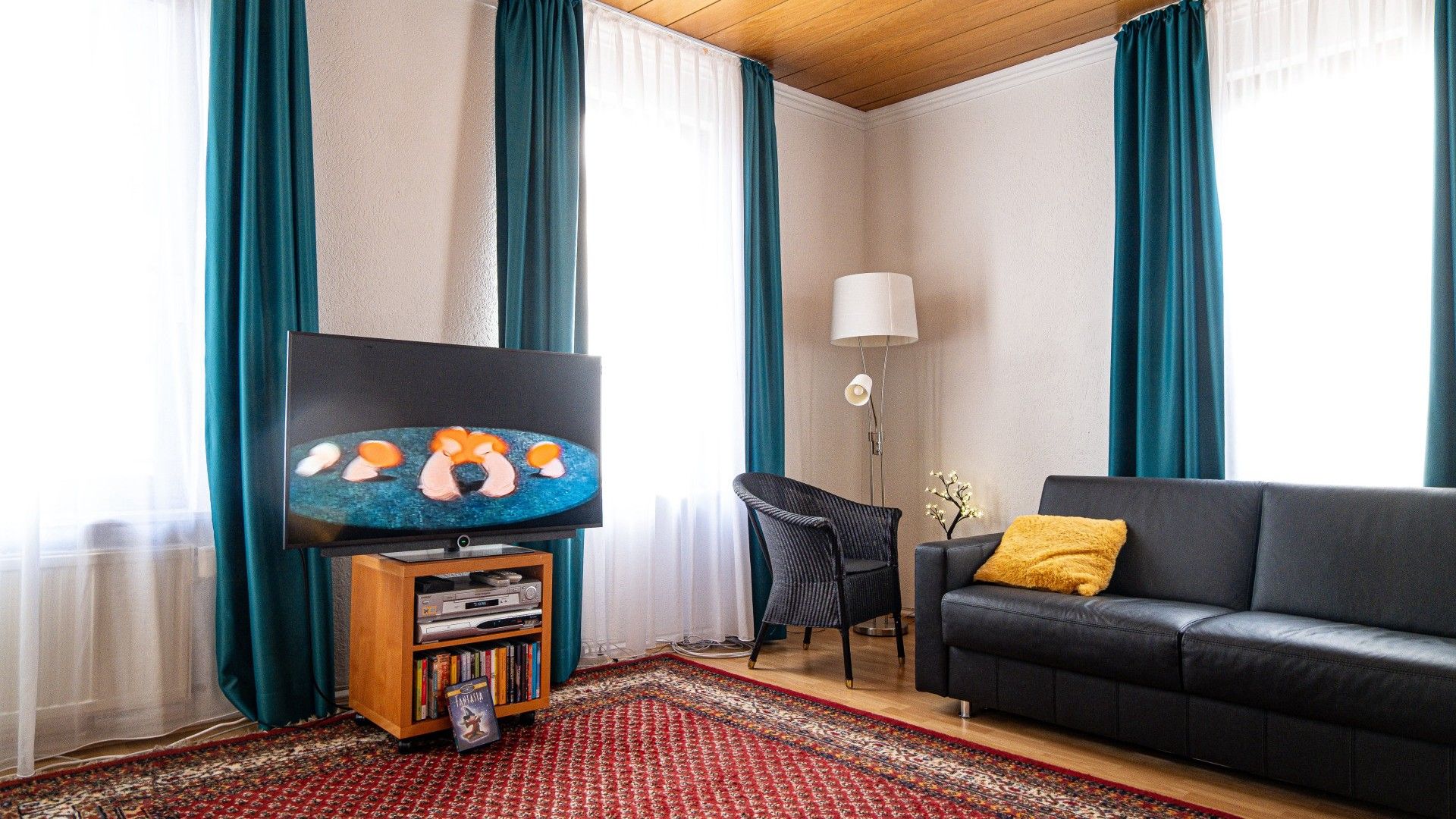 Ett vardagsrum med en tv, en soffa, en fåt ölj, en lampa och en bokhylla.