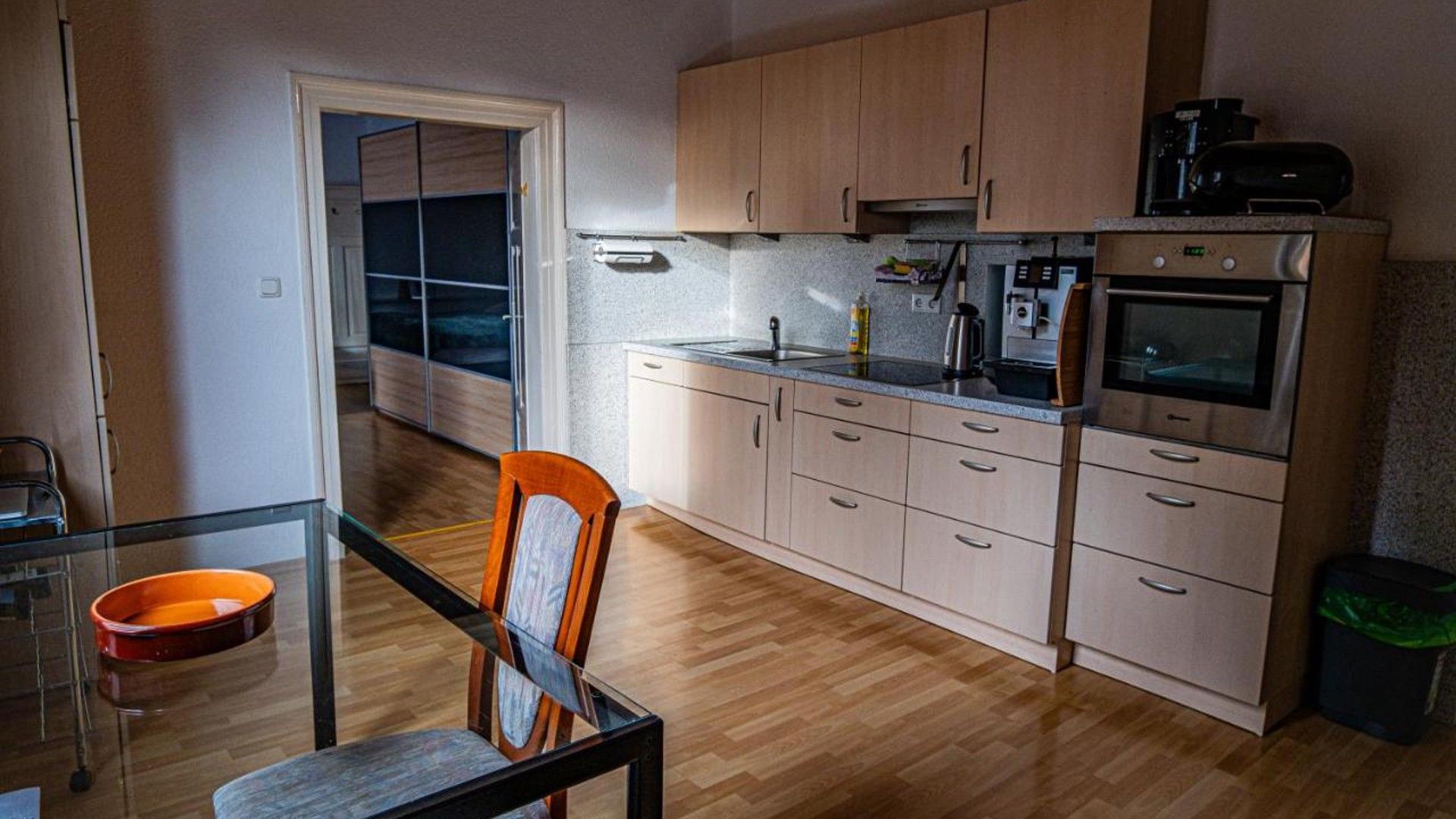 Eine kleine Küche mit Holzausstattung, einem eingebauten Backofen und einem Esstisch aus Glas.
