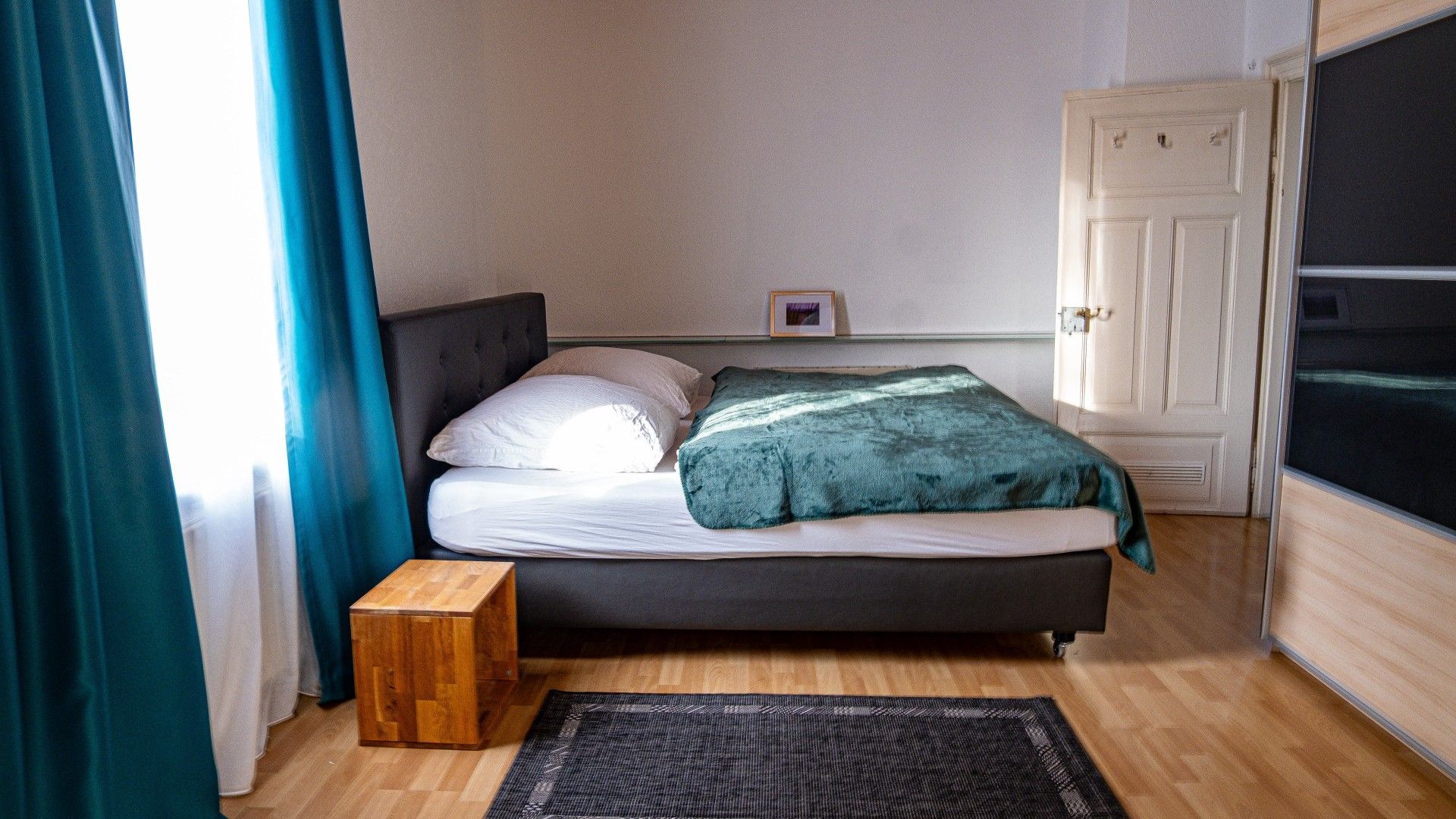 A bedroom with a bed, a bedside table, a door, and a window with curtains.