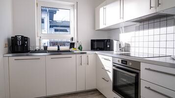 A modern kitchen with white cabinets, a stainless steel countertop, a built-in oven, a microwave, and a coffee maker.