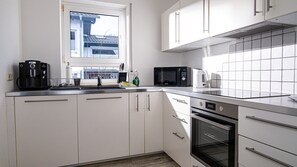 A modern kitchen with white cabinets, a stainless steel countertop, a built-in oven, a microwave, and a coffee maker. - Maisonette 1 Bad König – 90 m², Balcony (Bad König)