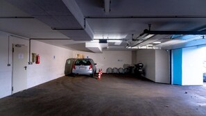 Eine Parkgarage mit einem Auto in der Mitte, einer blauen Tür rechts und einem Feuerlöscher an der Wand.