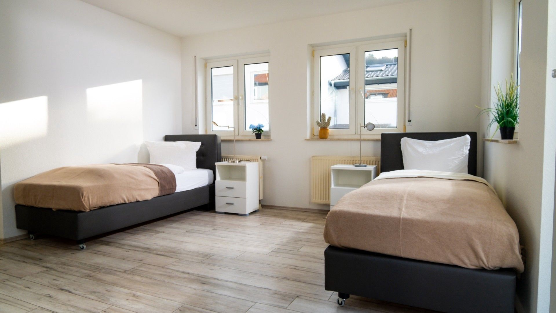 A bedroom with two beds, a radiator, a window with a view, and a small plant on the windowsill.