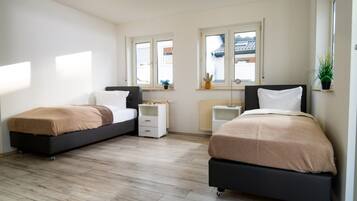 A bedroom with two beds, a radiator, a window with a view, and a small plant on the windowsill.