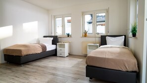 A bedroom with two beds, a radiator, a window with a view, and a small plant on the windowsill. - Maisonette 1 Bad König – 90 m², Balcony (Bad König)