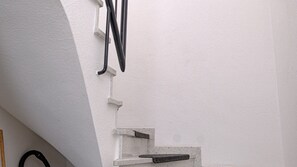 Eine Ecke eines Raumes mit einer weißen Wand, einem schwarzen Kabel und einem weißen Gegenstand, der vermutlich Teil der Raumstruktur ist.