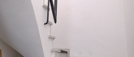 Una esquina de una habitación con pared blanca, un cable negro y un objeto blanco que parece ser parte de la estructura de la habitación.