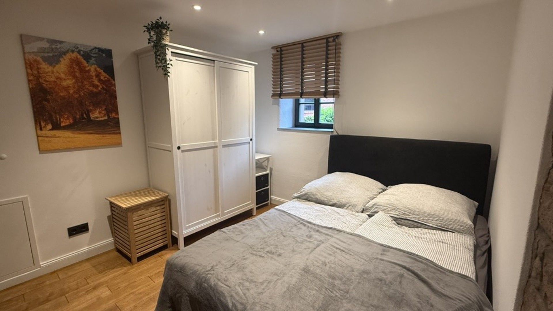 Ein Schlafzimmer mit einem Bett, einem Kleiderschrank, einem Fenster mit Jalousien und einem Bild an der Wand.