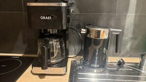 A coffee maker with a clear carafe and a black base, placed on a wooden countertop. - Alte Kammfabrik – Garden-Level Studio (Michelstadt)
