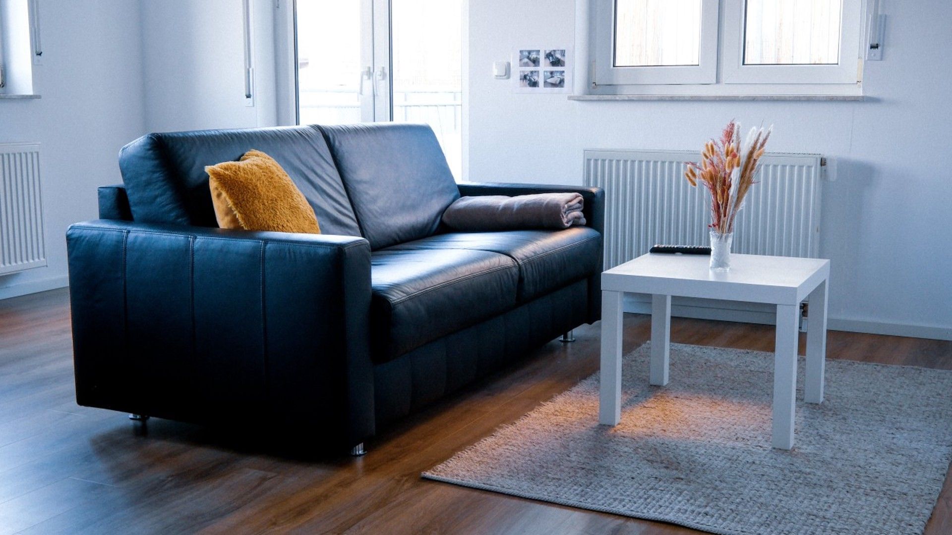 Un salon moderne avec un canapé en cuir, une table d’appoint blanche et un vase contenant des plantes séchées.