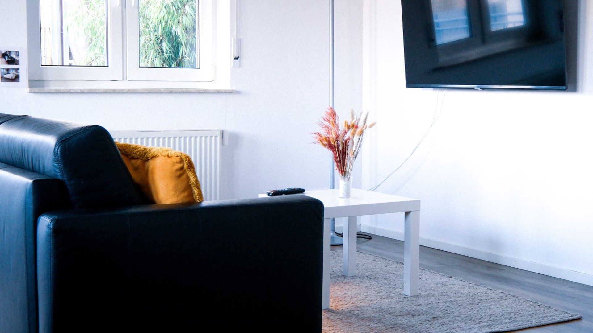 A modern living room with a black leather sofa, a white coffee table, and a flat-screen TV mounted on the wall.