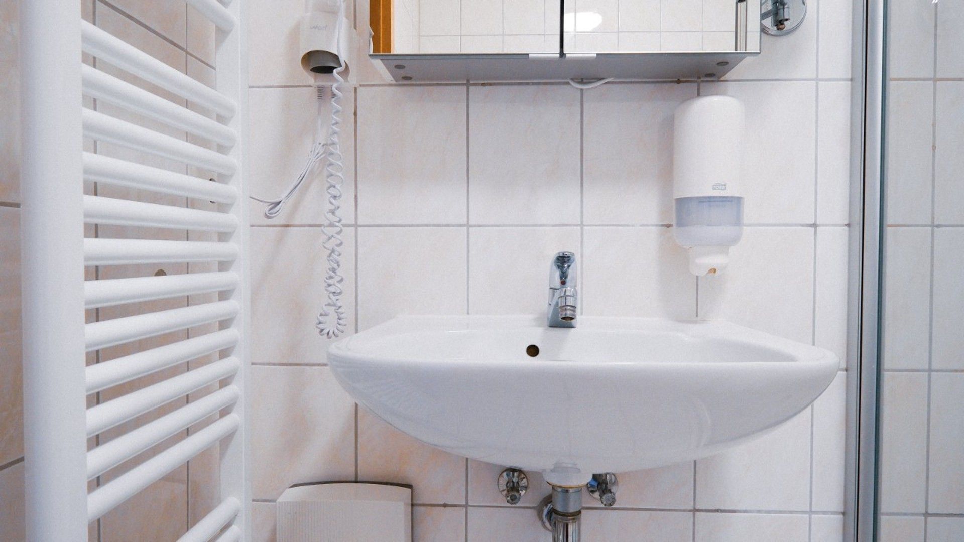 Ein Badezimmer mit einem weißen Waschbecken, einem Handtuchhalter, einem Spiegel und einer Seifenspender.