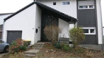 A two-story building with a white facade, a dark roof, and a small front porch with steps leading to the entrance.