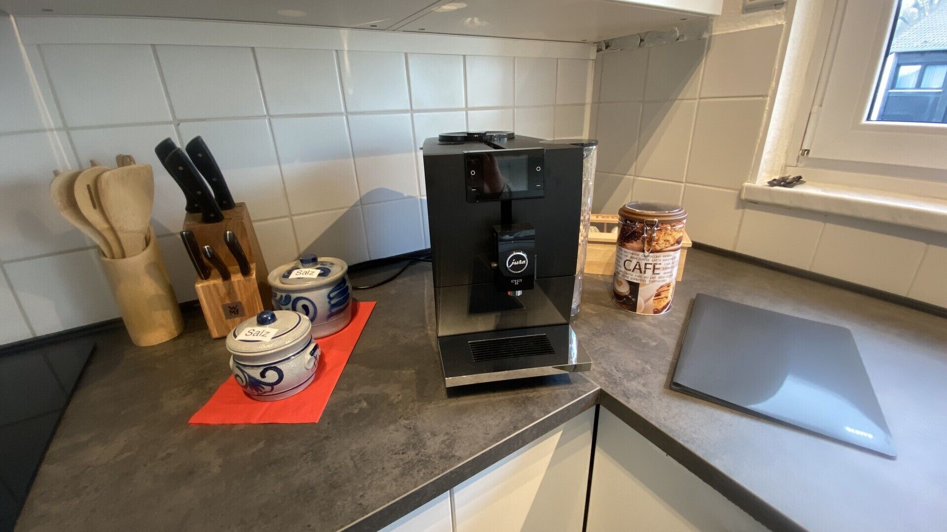 A kitchen with a coffee machine, jars labeled 'Salz,' a jar of 'CAFE,' and a cutting board.