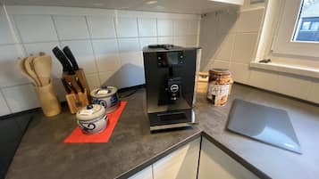A kitchen with a coffee machine, jars labeled 'Salz,' a jar of 'CAFE,' and a cutting board.