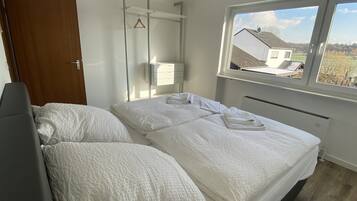 A bedroom with a bed, a bedside table, a hanging towel rack, and a window with a view of houses.