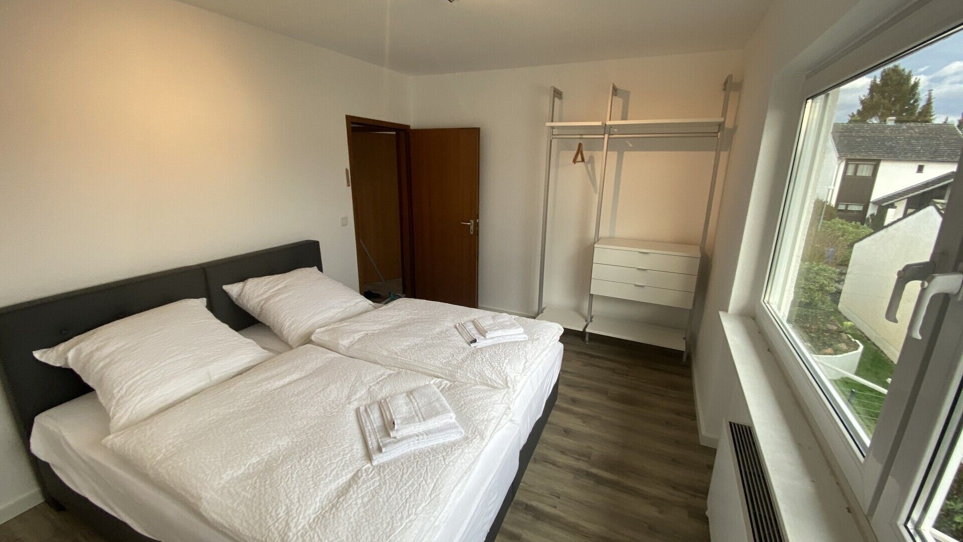A bedroom with two beds, a wardrobe, and a window with a view of houses.