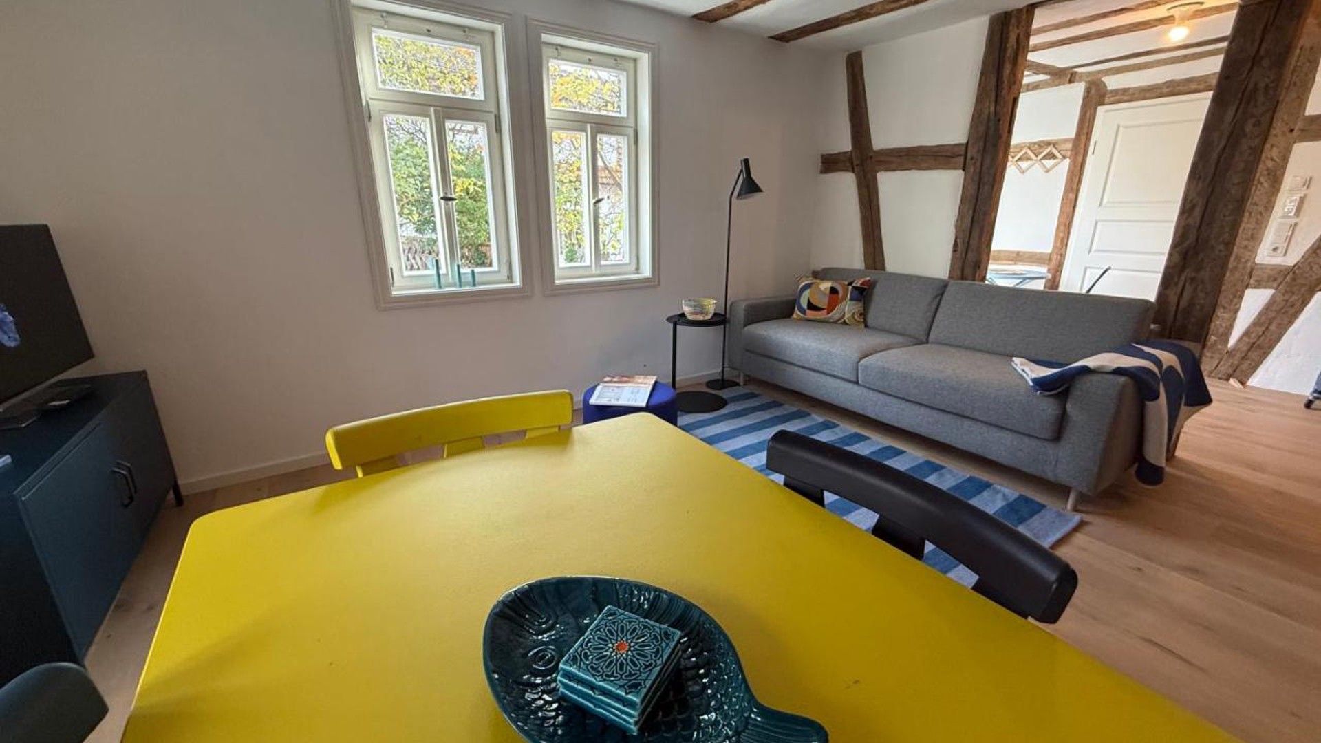 A room with a yellow table, a sofa, and a television on a cabinet.