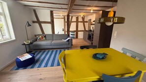 Ein Zimmer mit einem gelben Tisch, einem grauen Sofa, einem Streifen Teppich und freiliegenden Holzbalken an der Decke.