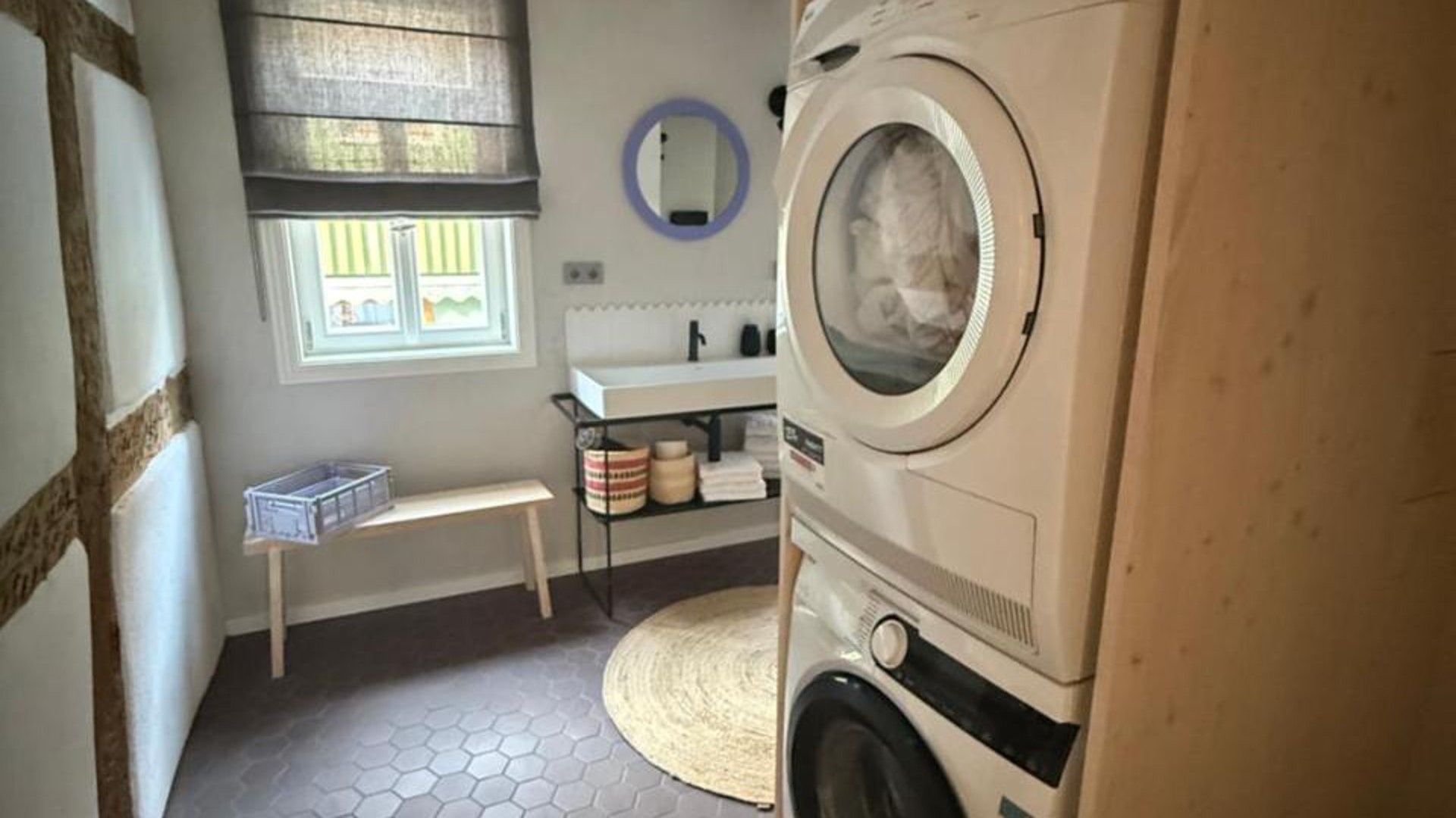 Ein Waschraum mit Waschmaschine, Waschbecken, Spiegel und einem Fenster mit Jalousien.