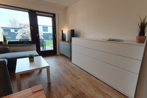 A modern living room with a sofa, a coffee table, a TV on a stand, and a large window. - Holiday apartment with 2 bedrooms (Cuxhaven)