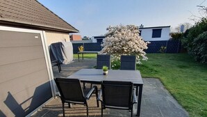 Eine Terrasse im Freien mit Tisch und Stühlen, einem überdachten Tisch, einem Blumentopf und einem blühenden Baum.